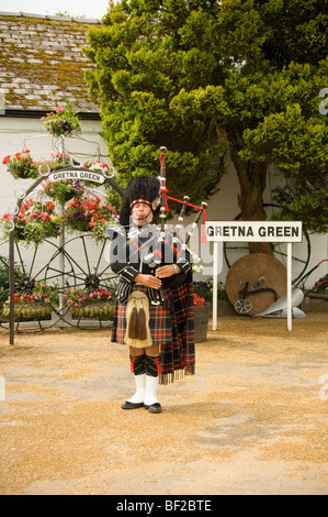 Kaukasischer schottischer Pfeifer, der vor dem Geschäft von Gretna Green Old Blacksmith, Schottland, Dudelsäcke spielt. VEREINIGTES KÖNIGREICH Stockfoto