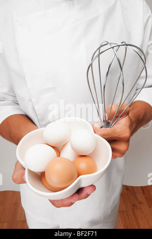 Mann hält eine Schale mit Eiern und einem Schneebesen Stockfoto