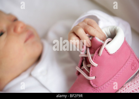 Babys erste Schuhe mit einem sehr jungen Baby Girl im Hintergrund unscharf. Stockfoto