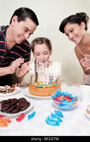 Mädchen Ausblasen Geburtstag Kerze mit ihren Eltern Stockfoto