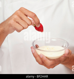 Mann eine Erdbeere in Creme Dippen Stockfoto