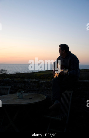 Mann spielt Gitarre mit Blick auf Sonnenuntergang Meer Stockfoto