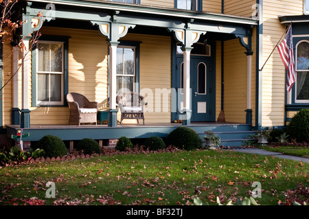 Viktorianische Fronteinstieg Veranda Akzenten in grün mit bequemen Korbsesseln & fliegenden amerikanische Flagge in der Stadt Montgomery New York Stockfoto