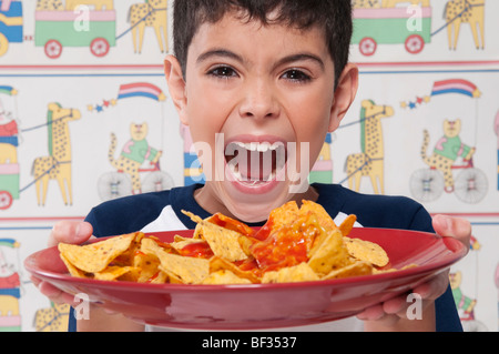 Bildnis eines Knaben halten eine Platte mit Nachos und schreien in Aufregung Stockfoto