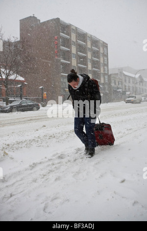 Eine junge Frau zu Fuß und ziehen ihren Fall entlang einer Straße in einen ordentlichen Schneesturm in Montreal. Stockfoto