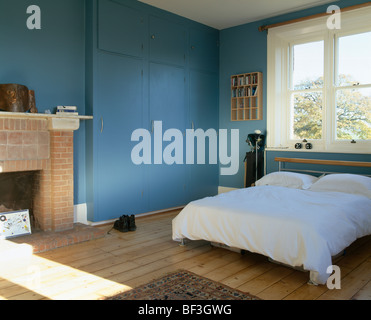 Weiße Bettwäsche auf Bett im blauen Schlafzimmer mit Holzboden und großen blauen montierten Schrank Stockfoto