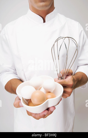 Mann hält eine Schale mit Eiern und einem Schneebesen Stockfoto