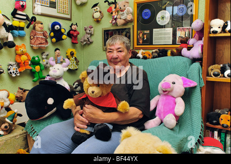 Ältere Frau mit ihrer weichen Spielzeug-Kollektion in ihrem Wohnzimmer sitzen Stockfoto