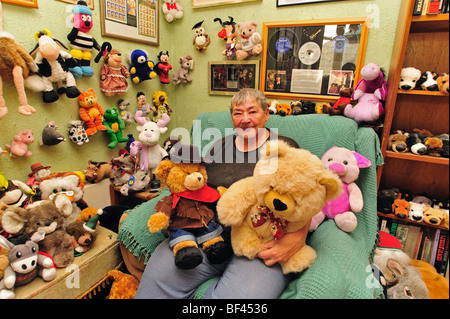 Ältere Frau mit ihrer weichen Spielzeug-Kollektion in ihrem Wohnzimmer sitzen Stockfoto