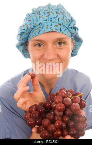 ziemlich glücklich und lächelnd zuversichtlich Krankenschwester fördern gesunde Ernährung mit frischem Obst Trauben während des Tragens Krankenschwester Peeling Kleidung Stockfoto