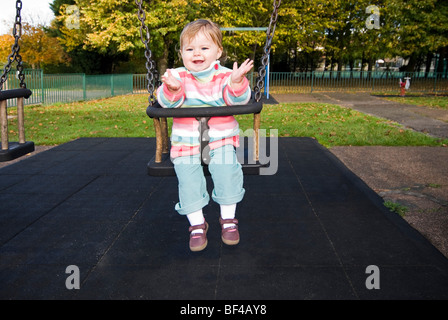 Horizontale Nahaufnahme Portrait eines kleinen Mädchens lächelnd und klatschten im Park in der Sonne auf einer Schaukel sitzend. Stockfoto