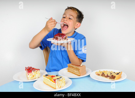 Junge, Kuchen essen, an einem Tisch mit vier Platten mit anderen Stücke des Kuchens Stockfoto