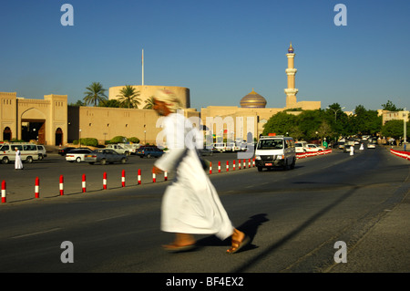 Arabische Mann tragen traditionelle Dishdash Kleidung laufen vor einem herannahenden Auto auf der Straße, Nizwa, Sultanat Oman, Stockfoto