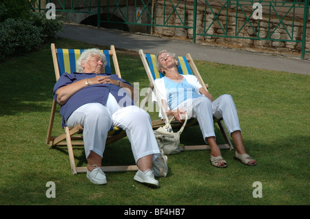 zwei ältere Damen, die ein Sonnenbad im Liegestuhl, senken Sie Gärten, Bournemouth, Dorset, England, UK Stockfoto