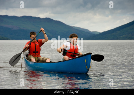 Junge kaukasische Männer und Frauen in roten Schwimmwesten paddeln auf Loch Earn, Perthshire, Schottland, ein blaues kanadisches Kanu. VEREINIGTES KÖNIGREICH Stockfoto