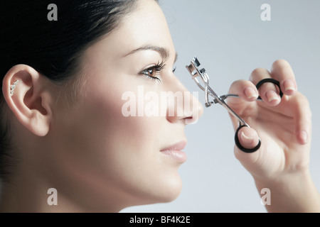 Junge dunkelhaarige Frau gestalten ihre Wimpern mit einer Wimpernzange, Schönheit Stockfoto