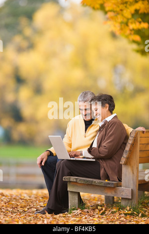 African Paar mit Laptop auf der Parkbank im Herbst Stockfoto