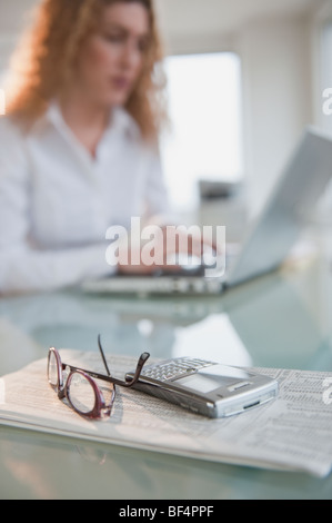 Hispanic Frau mit Laptop in der Nähe von Zeitung, Handy und Brillen Stockfoto