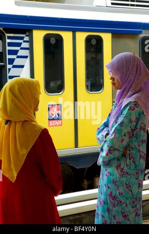 Bunte PendlerInnen islamischen Hijab chatten, wie sie an einer Station warten. Kuala Lumpur, Malaysia Stockfoto