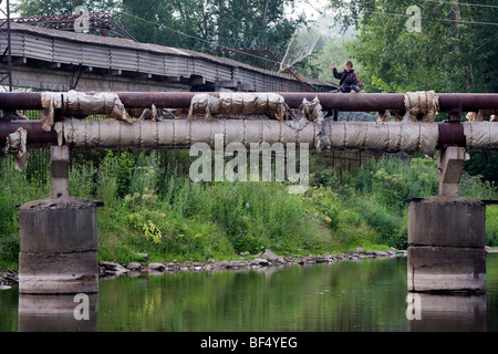 Junge sitzt auf Industrial Pipe Systems der verlassenen Fabrik auf der anderen Flussseite, Tagil, Ural, Russland Stockfoto