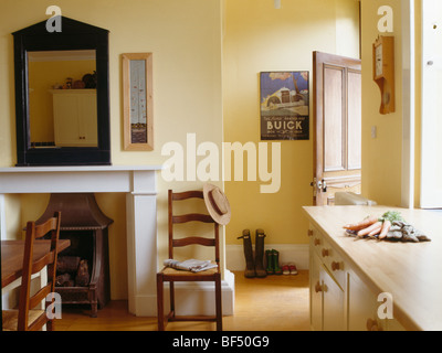 Antiker Holz Spiegel über dem Kamin im kleinen traditionellen blass gelbe Küche Esszimmer mit Ladder-back Stühle Stockfoto