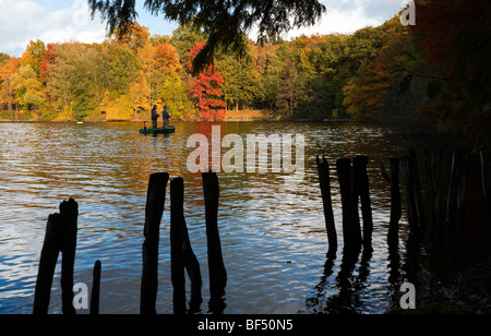 zwei Angler in einem Boot auf einem See. herbstliche Bäume am Ufer, Silhouette bleibt von einem Steg im Vordergrund Stockfoto