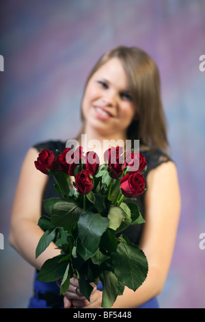 Porträt einer jungen Frau, die lächelt und einen Strauß roter Rosen in der Hand hält, Großbritannien. Stockfoto