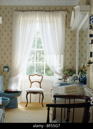Antiker Stuhl vor hohen Fenster mit weißen Voile Vorhänge im traditionellen Badezimmer mit gemusterten Tapeten Stockfoto