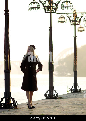 Schöne blonde Dame in Barett bleiben unter Laternen auf promenade Stockfoto