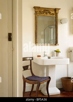 Antiken georgischen goldgerahmten Spiegel über weißen Sockel Becken im Stadthaus Badezimmer mit antiken Stuhl Stockfoto