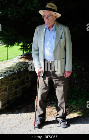 Ein älterer Mann, steht im Schatten einer Eibe, mit einem Gehstock und einen Panama-Hut. Stockfoto