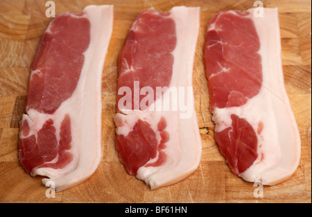 drei Streifen roh zurück Speck aus organischen britische Saddleback Schweine aufgezogen in Irland auf einem hölzernen Metzger Block angelegt Stockfoto