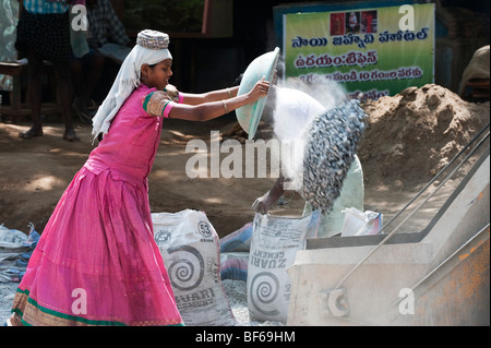 Junge indische Frau arbeiten auf den Straßen werfen Schale, Steine, die zu einem Betonmischer. Puttaparthi, Andhra Pradesh, Indien Stockfoto