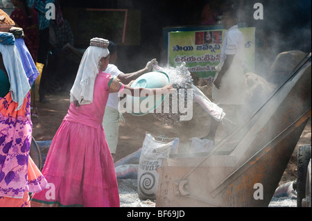 Junge indische Frau arbeiten auf den Straßen werfen Schale, Steine, die zu einem Betonmischer. Puttaparthi, Andhra Pradesh, Indien Stockfoto