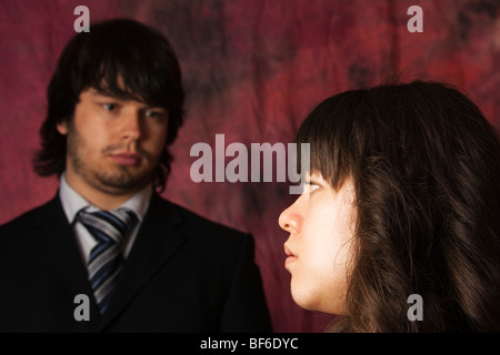 Junge Frau sucht jungen Mann in einem dunklen Anzug hinter ihr. Die Vordergrund-Frau im Mittelpunkt. Stockfoto