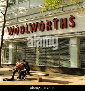 zwei Jugendliche sitzen auf einer Bank vor einem stillgelegten Zweig der Woolworths speichern Swansea Stadtzentrum Wales UK Stockfoto