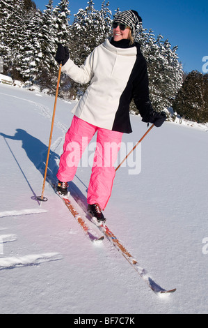 Frau in rosa Snowboardhosen machen Langlaufen auf einem See unter blauem Himmel Stockfoto