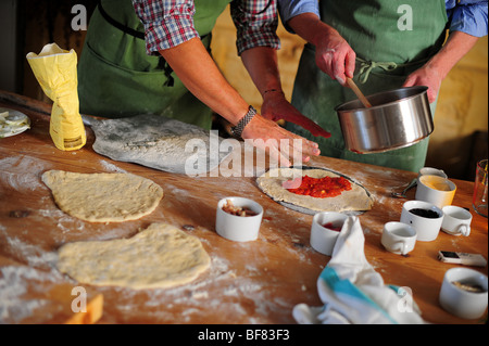 Hinzufügen von Tomatensauce zu Hause Pizza auf einem Küchentisch gemacht Stockfoto