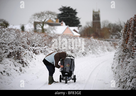 eine Mutter, die zu Fuß ein Baby unten einen Feldweg in den Schnee, in hohen Bickington, Devon Stockfoto