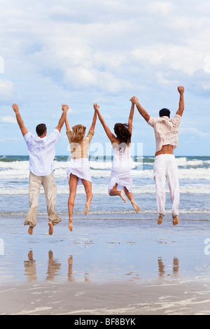 Vier junge Leute, zwei Paare Hand in Hand, Spaß und springen in der Feier an einem Strand Stockfoto