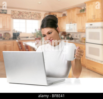 Schöne junge Frau hält Kaffee während der Arbeit an ihrem Laptop-Computer Stockfoto