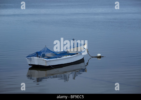 Eine kleine Altern Fischerboot in ruhigen Gewässern verankert. Stockfoto