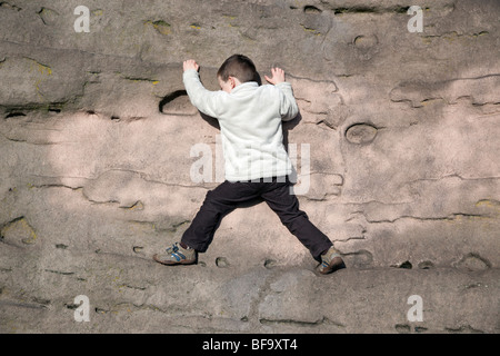Ein kleiner Junge auf eine Praxis, die Felsen zu klettern. Stockfoto