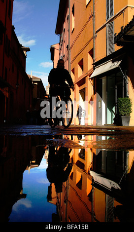 Ein Silhouette Mann Zyklen vorbei an Pfützen in den bunt bemalten Straßen von Bologna in Italien, Europa Stockfoto