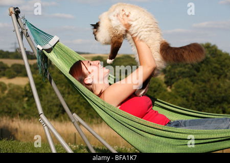 Heiligen Katze von Birma, Birma (Felis Silvestris F. Catus), junge Frau liegen in der Hängematte ein Kater mit in die Luft hält eine Stockfoto