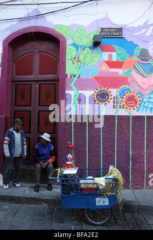 Mann, Verkauf von Orangensaft aus Warenkorb vor Handwerksladen mit Wandbild auf Wand, Calle Linares, La Paz, Bolivien Stockfoto