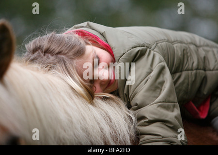 inländische Pferd (Equus Przewalskii F. Caballus), Mädchen sitzen auf einem Pferd, lächelnd und legen ihren Kopf auf seine Mähne, Deutschland Stockfoto