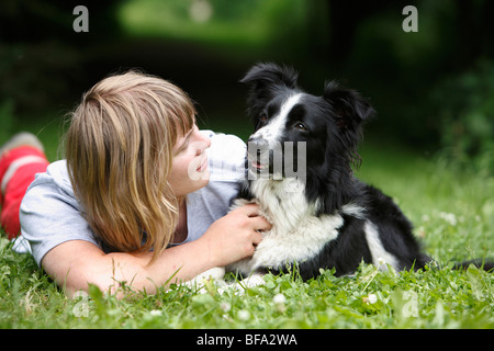 Mischling Hund (Canis Lupus F. Familiaris), Trainer liegend auf dem Bauch streichelt einen Hund Border Collie-Terrier-Mix, auf einer Wiese Stockfoto