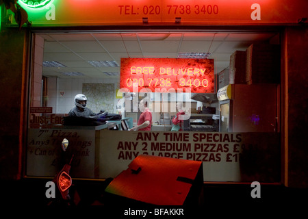 Ein Lieferung Fahrer sammelt Aufträge in der Nacht bei einem Take-away Pizza-Geschäft in Herne Hill, London. Stockfoto