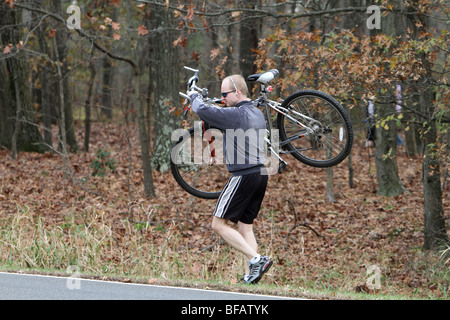 Ein Mann mit seinem Mountainbike aus dem Wald. Das Fahrrad steht ganz oben auf seiner Schulter. Stockfoto